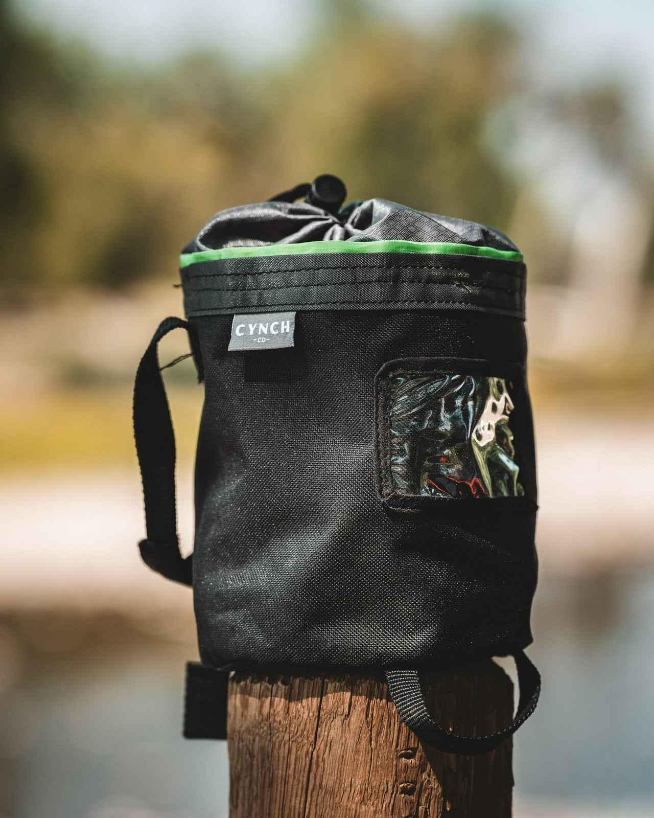 Green-trim CYNCH bag on a wooden post by the water